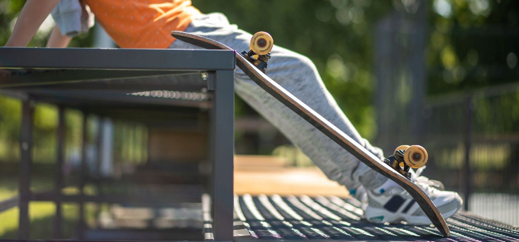 Junge Person sitzt neben einem Skateboard auf einer Bank