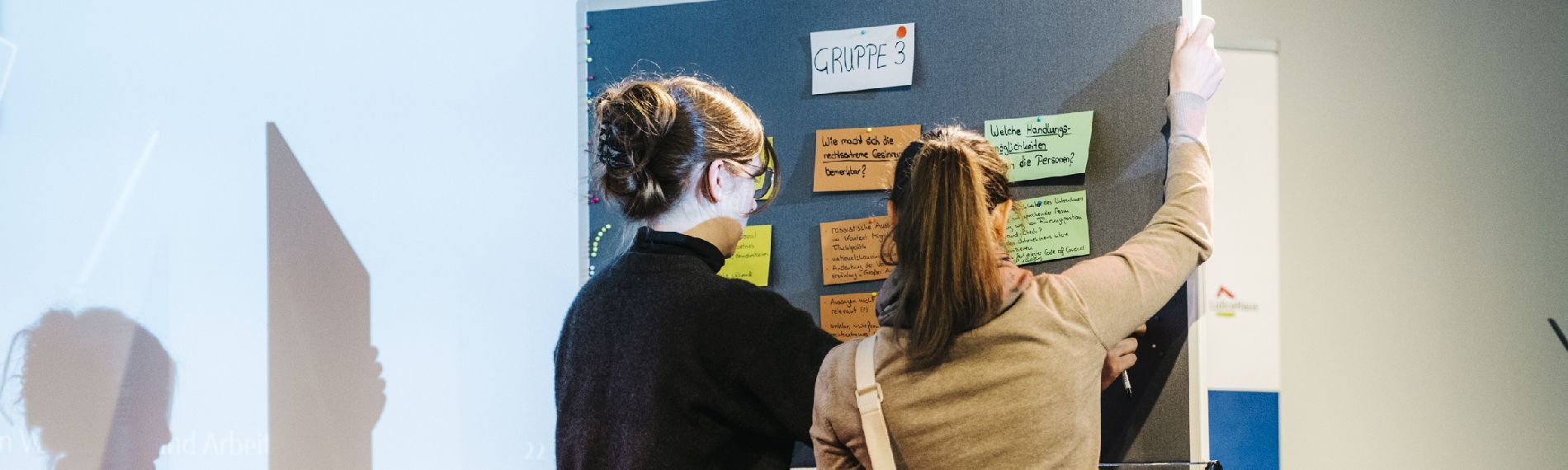 Teilnehmende eines Workshops pinnen Karten an eine Stellwand